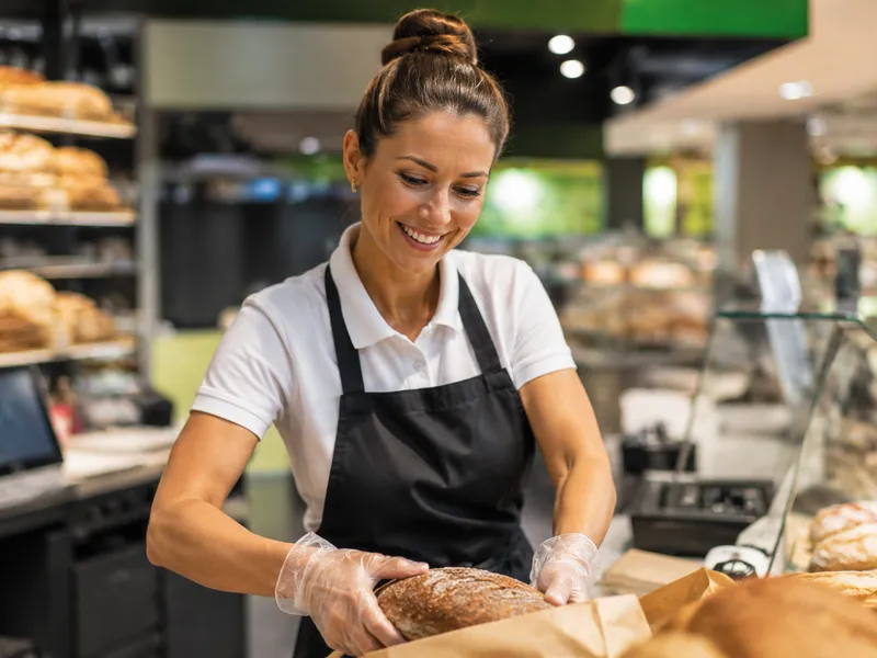 Vendedora en el comercio minorista de alimentación con un certificado sanitario digital en el smartphone